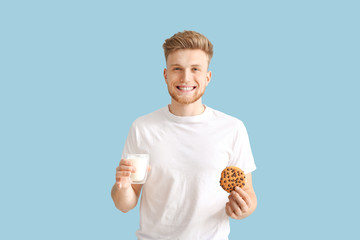 Wall Mural - Handsome young man with tasty cookie and glass of milk on color background