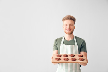 Wall Mural - Handsome male baker holding board with fresh cookies on light background