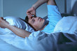 Young man suffering from insomnia while lying in bed at night