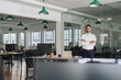 © mavoimages - Young businessman smiling while standing in a large modern office