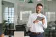 © mavoimages - Smiling businessman using a tablet in a large modern office