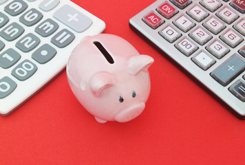 Piggy bank between two calculators on red background, save money concept