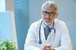 © goodluz - Portrait of handsome mature doctor sitting at desk in modern office