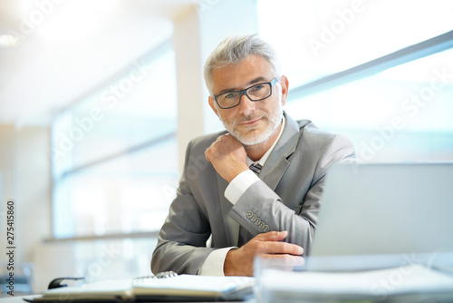 Stampa su Tela  Portrait of mature businessman sitting in office looking at camera