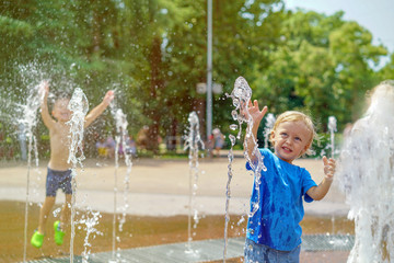 A boy playing with water in park fountain. Hot summer. Happy young boy has fun playing in water fountains