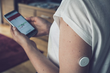 Wall Mural - Woman checking glucose level with a remote sensor and mobile phone, sensor checkup glucose levels without blood. Diabetes treatment. Focus on foreground.