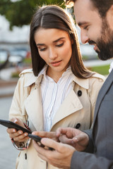 Sticker - Photo of serious office workers man and woman holding takeaway coffee while using mobile phones on city street