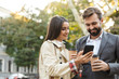 © Drobot Dean - Photo of joyous office workers man and woman holding takeaway coffee while using mobile phone on city street