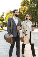 Wall Mural - Full length photo of cheerful office workers man and woman holding takeaway coffee while walking on city street