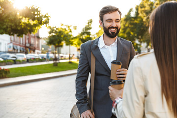 Poster - Photo of happy office workers man and woman drinking takeaway coffee while speaking on city street