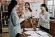 © PR Image Factory - Young creative team work colleagues ladies discussing ideas in board room. Group of asian female people during start up business meeting in studio. three coworkers girls laughing and talking.