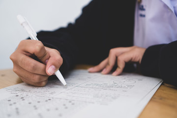 Wall Mural - Education test exam concept, high school / university student holding pencil writing paper answer sheet on lecture chair for taking exams in examination room or classroom. Educational assessment ideas