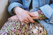 © Axel Bueckert - mid section of young woman wearing denim jacket over summer dress with floral pattern - close-up of female hands folded in her lap