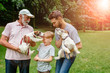 © Iryna - Multigenerational family walking with dog. Dad, granddad holds Jack russel terrier, their son having fun, laughing, kissing, walking together in green meadow on park outdoor.