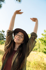 Poster - Photo of happy brunette woman wearing stylish hat and eyeglasses walking in green park on sunny day