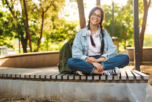 Positive Happy Cute Young Student Girl Wearing Eyeglasses Sitting On Bench Outdoors In Nature Park.