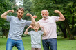 © Iryna - Portrait og happy family - grandpa, father and his son smiling and showing their muscles outdoor in park on background. Three different generation concept.