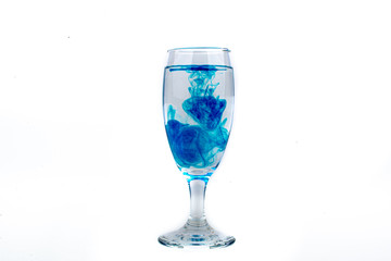 Blue food coloring diffuse in water inside wine glass with empty copyspace area for slogan or advertising text message, over isolated white background.