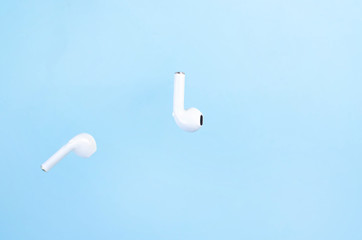 Cordless white headphones in the air on a blue background.