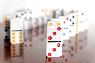 Vertically standing white dominoes stand in a row. Playing dominoes on a wooden table. The concept of the game of dominoes. A symbol of excitement, overcoming difficulties in business.