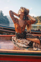 fashionable young model in boho style dress on boat at the lake