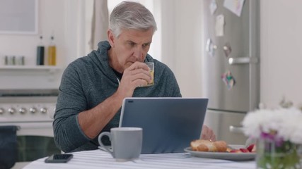 happy mature man using laptop computer at home drinking juice typing messages browsing online enjoying working in morning at breakfast 4k footage