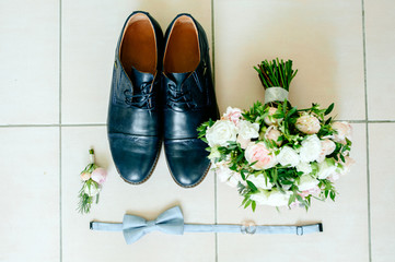 Stylish men's shoes on a dark wooden table next to the shoes is a pink butterfly, a boutonniere with live roses and a mechanical clock, the groom is ready for the wedding