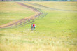© GMars - Two young girls with backpacks and photo camera make selfie on phone near rural road. Horse farm pasture with mare and foal. Small village with old houses. Summer landscape with green hills