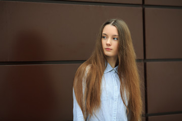 Portrait of a young pretty caucasian teenage girl with long hair in a blue shirt opposite brown background. Close up.