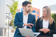 © Mangostar - Two business partners watching presentation and discussing project. Man and woman sitting outdoors, holding laptop and talking. Business communication concept