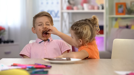 Happy sister feeding brother smeared with chocolate, sugar overeating, caries