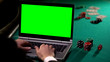 © motortion - Male gambler betting poker online on laptop, holding lucky dice, green screen