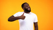 © motortion - Young bearded black guy showing thumbs up, smiling on camera yellow background