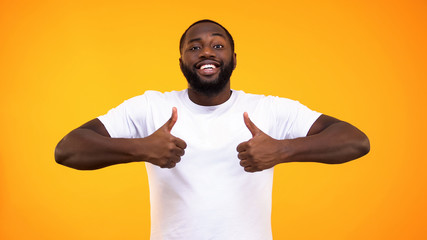 Wall Mural - Handsome black man smiling confidently, showing thumbs up on yellow background