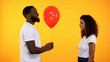 © motortion - Happy boyfriend giving red balloon to girlfriend on orange background, date