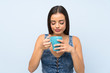 © luismolinero - Young woman over isolated blue wall holding hot cup of coffee