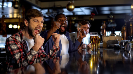 Joyful multiracial friends cheering for favorite team in bar, celebrating goal