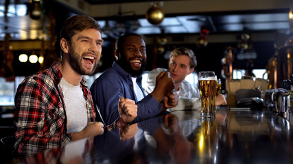 Multiracial male friends celebrating victory, cheering for favorite team in bar