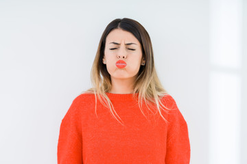 Sticker - Young woman wearing casual red sweater over isolated background puffing cheeks with funny face. Mouth inflated with air, crazy expression.