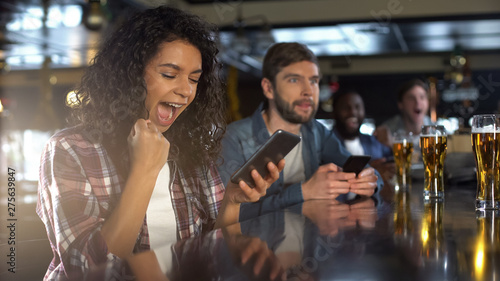 Cuadros en Lienzo Cheerful biracial lady in pub celebrating successful bet on sports, online app