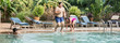 Three happy teenager brothers and sister are jumping into infinity swimming pool at the resort