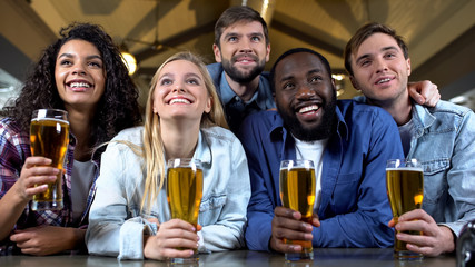 Multi-ethnic friends watching tv program on big screen in beer bar, leisure