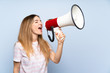 © luismolinero - Young woman over isolated blue background shouting through a megaphone
