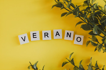 The inscription verano in spanish on the letters of the keyboard on a yellow background with branches of flowers