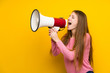 © luismolinero - Young woman with long hair over isolated yellow wall shouting through a megaphone
