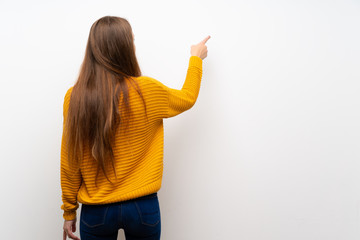 Young woman with yellow over isolated white wall pointing back with the index finger