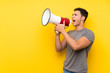 © luismolinero - Handsome man over isolated yellow wall shouting through a megaphone