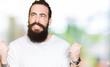 © Krakenimages.com - Young hipster man with long hair and beard wearing casual white t-shirt very happy and excited doing winner gesture with arms raised, smiling and screaming for success. Celebration concept.