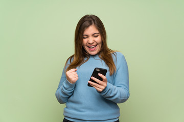 Young girl over green wall with phone in victory position