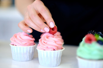 Close up of female hand topping a cupcake with refreshing mint leaf or picking it. Pastry chef woman making sweet dessert cake. Horizontal image